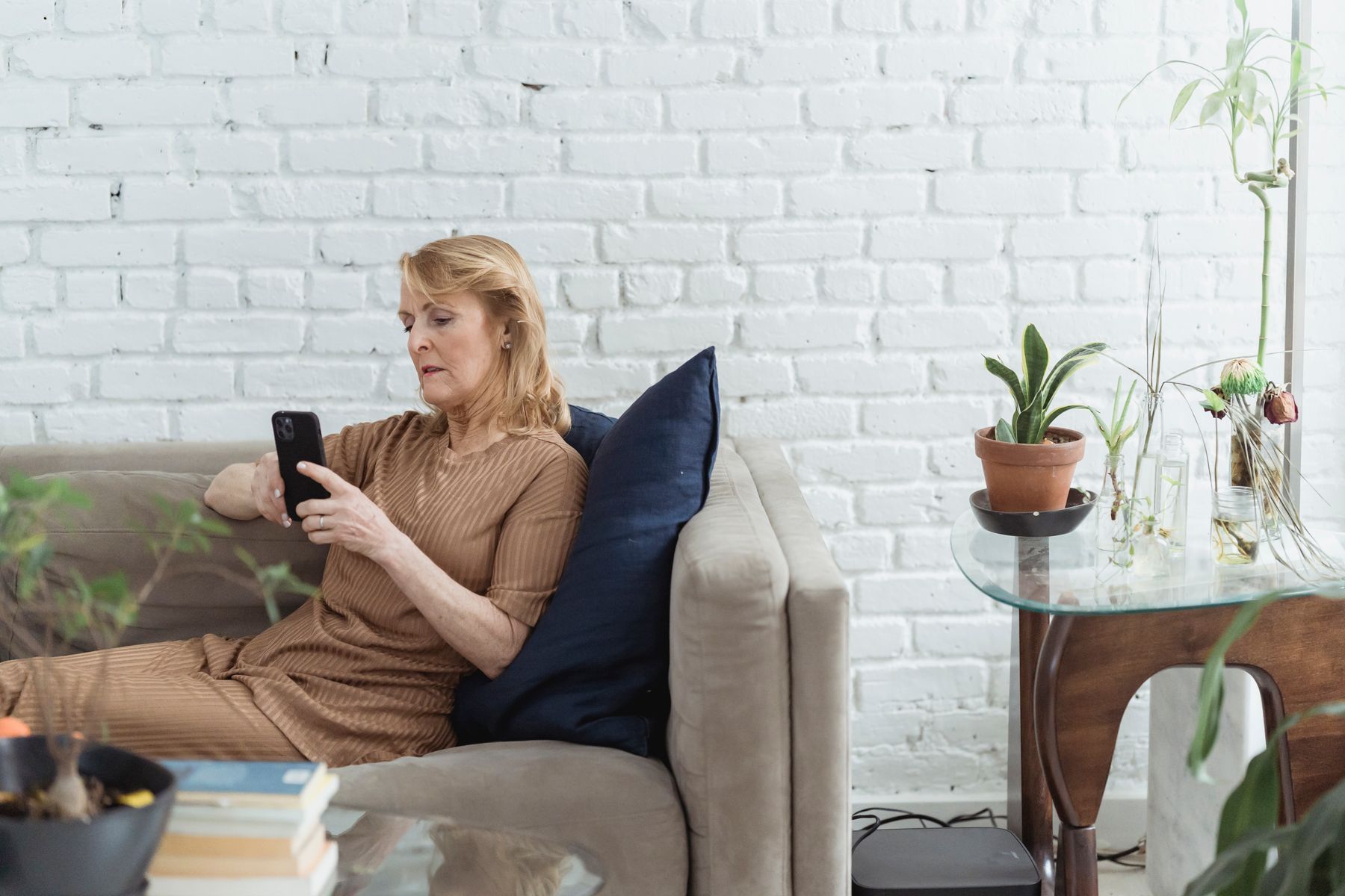 Une femme consulte son téléphone, assise dans son salon.